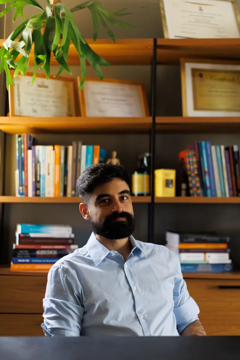 Júlio em frente à estante de livros e certificados do consultório
