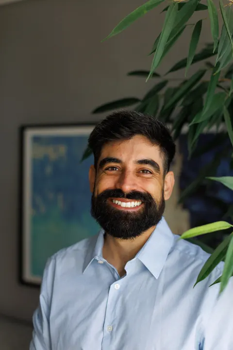 Júlio sorrindo, de camisa azul-clara, entre as plantas do consultório